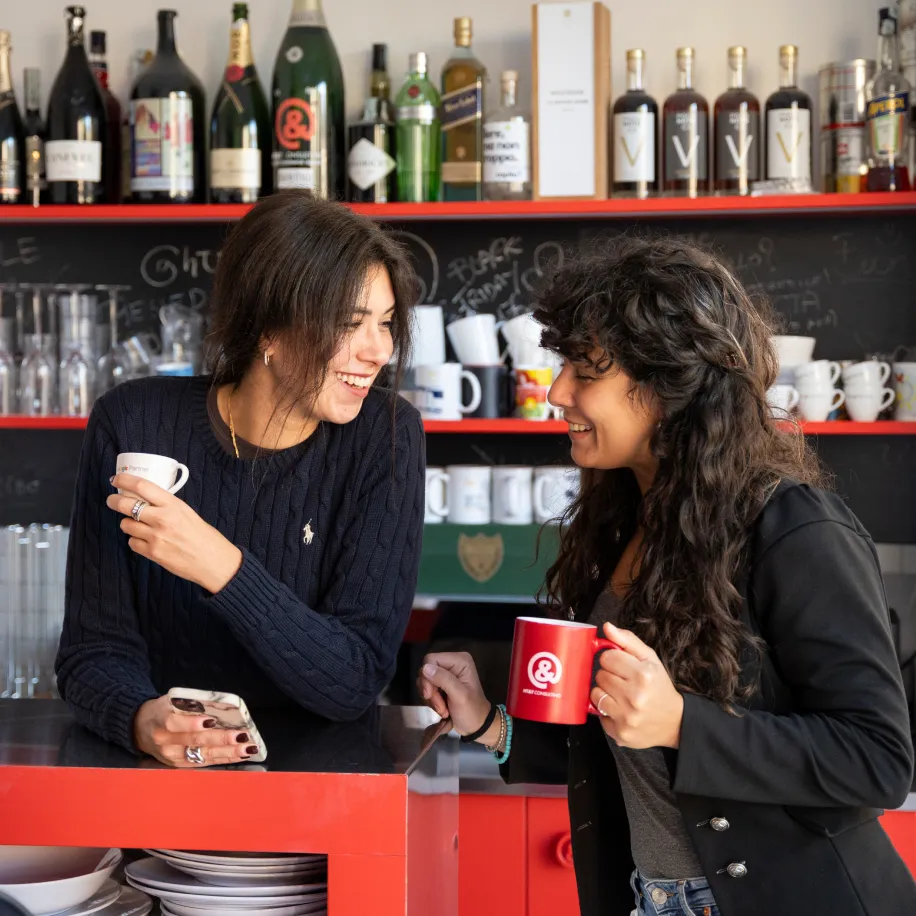 Immagine di due colleghe che sorridono e conversano bevendo un caffè al bar della zona relax dell'ufficio